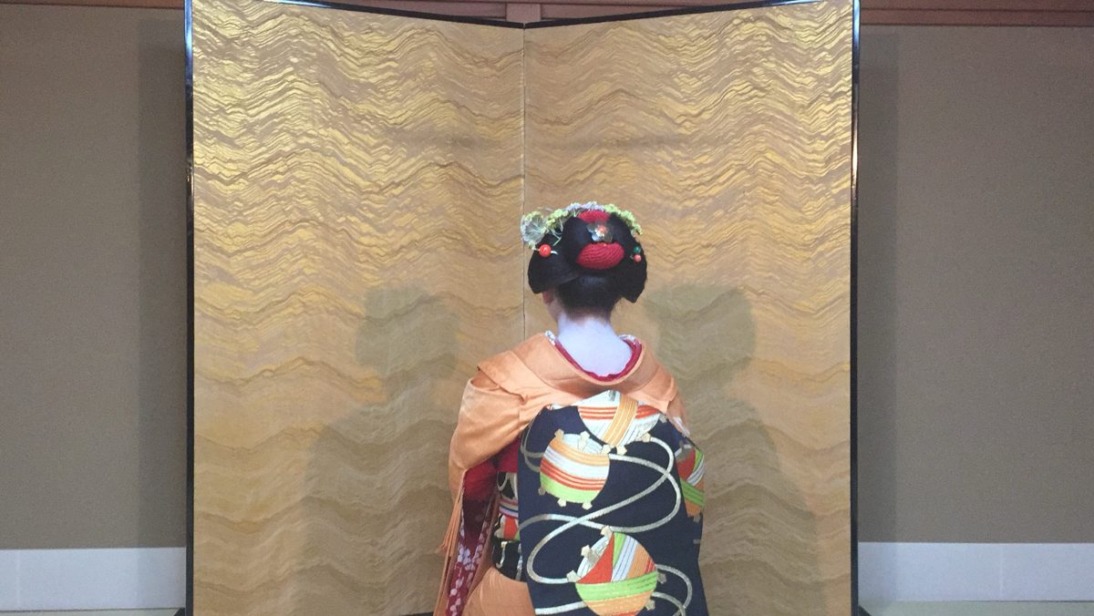 金屏風の前に座る舞妓の後ろ姿