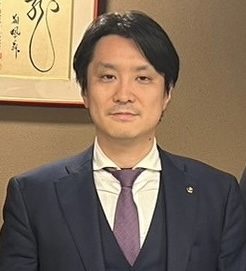 紫のネクタイのスーツ姿の種田成昭