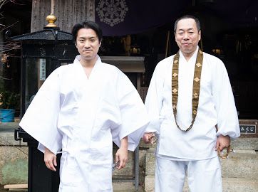 白衣を着て僧侶と並ぶ種田成昭